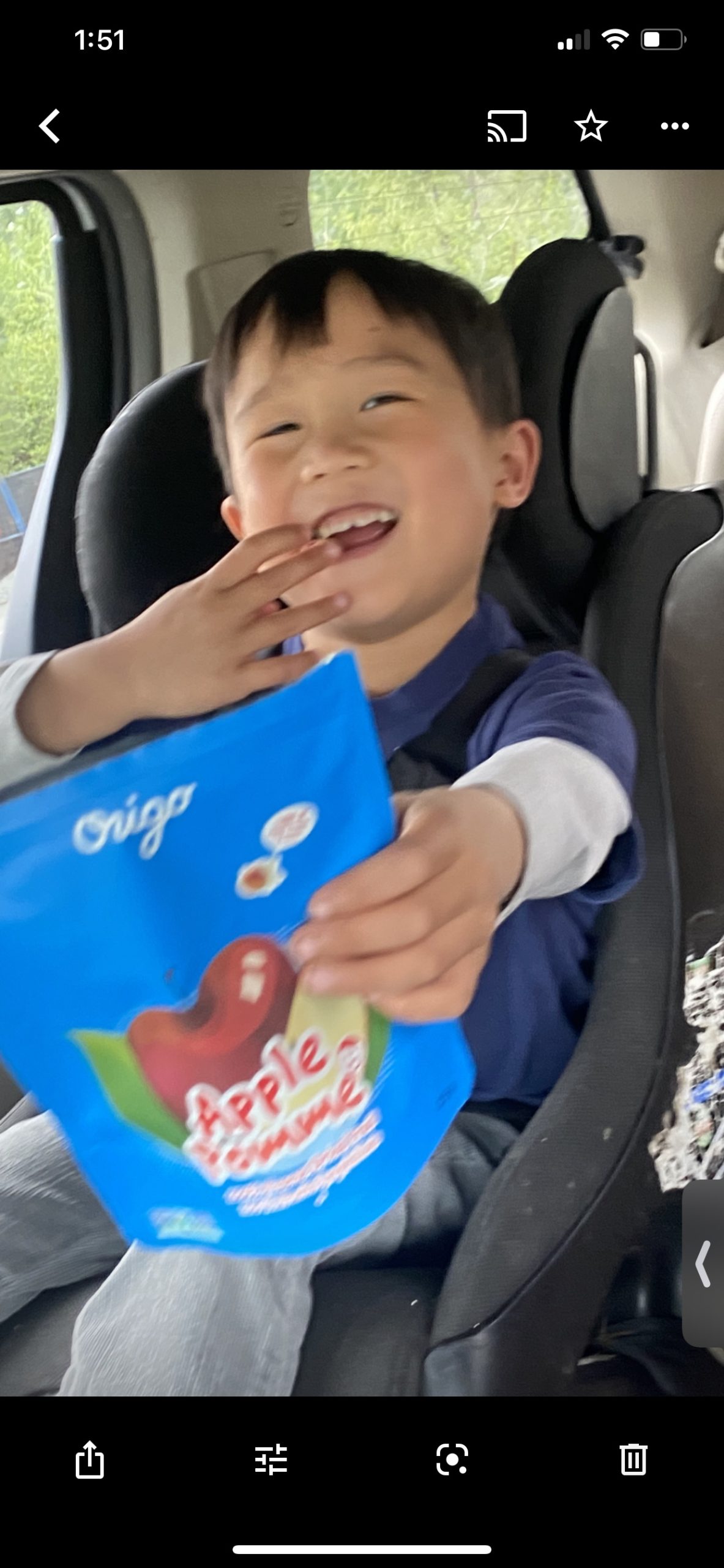 A smiling child in a car seat holding an Origo Apple freeze-dried fruit pouch