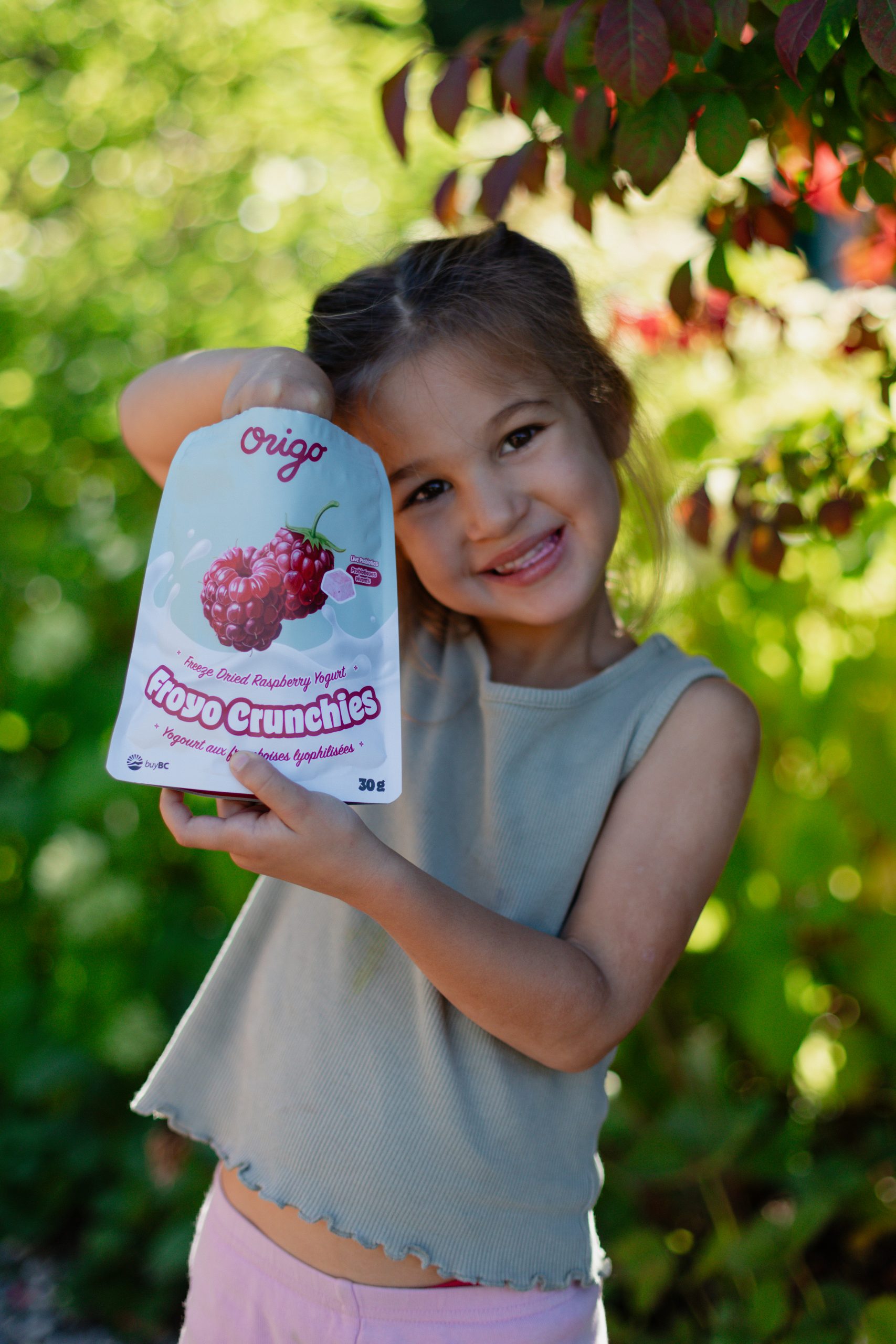 Smiling child outdoors holding a pouch of Origo Raspberry Froyo Crunchies