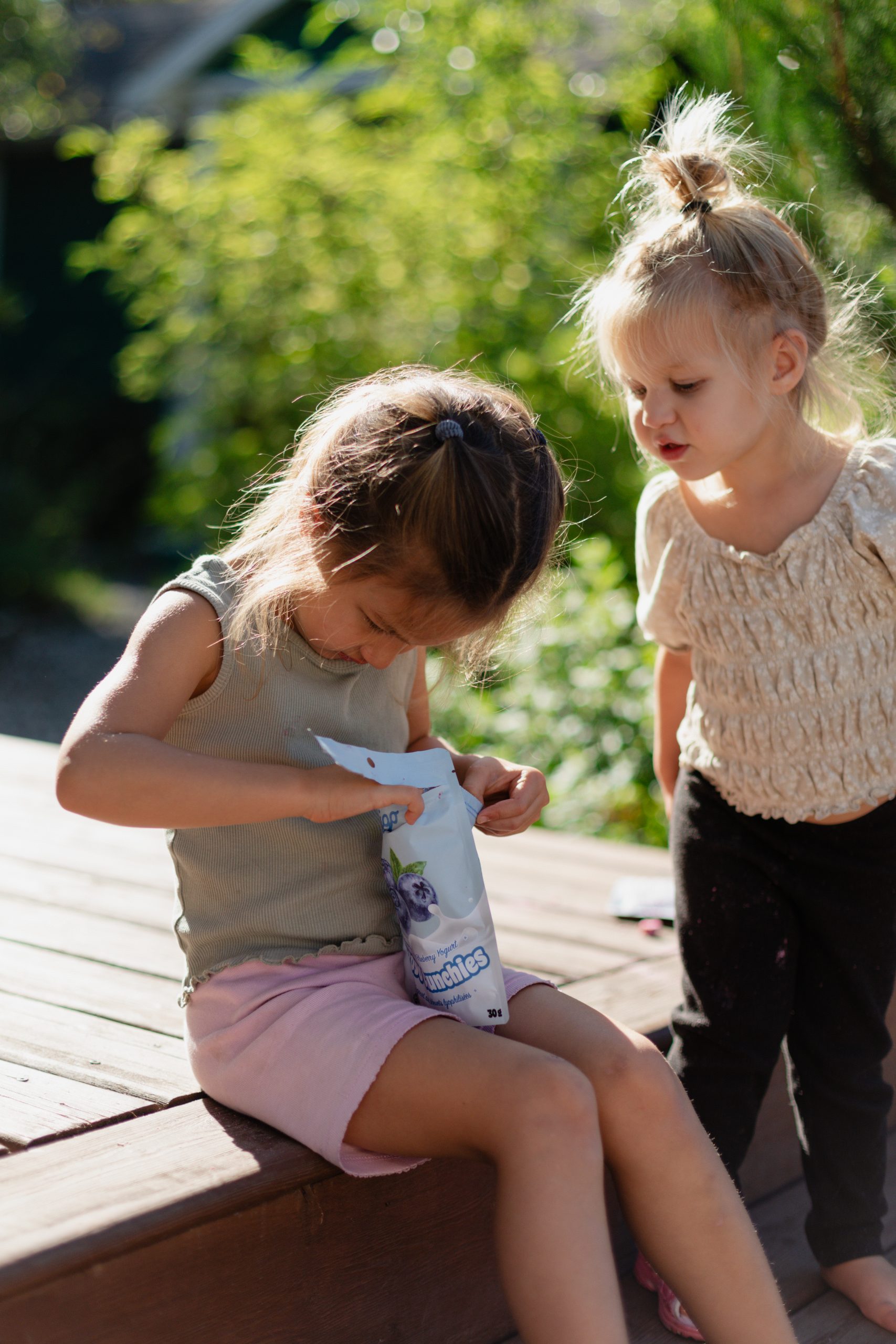 Two children outdoors sharing a pouch of Origo Blueberry Froyo Crunchies