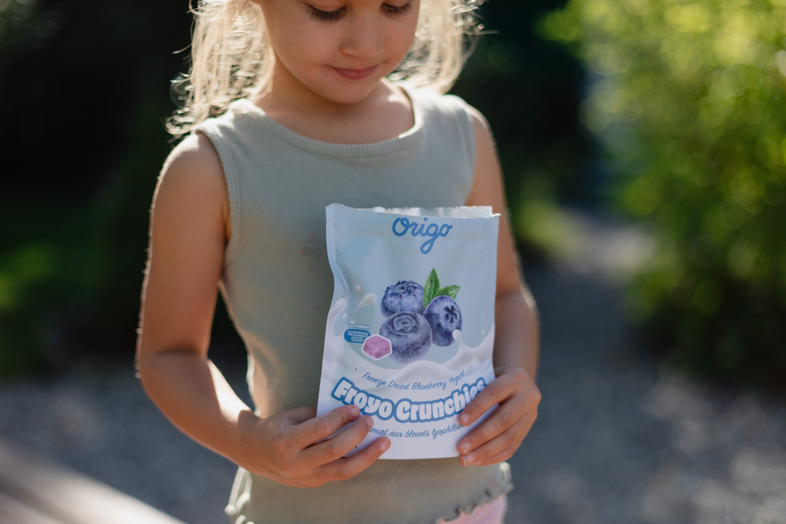 Child outdoors holding a pouch of Origo Blueberry Froyo Crunchies