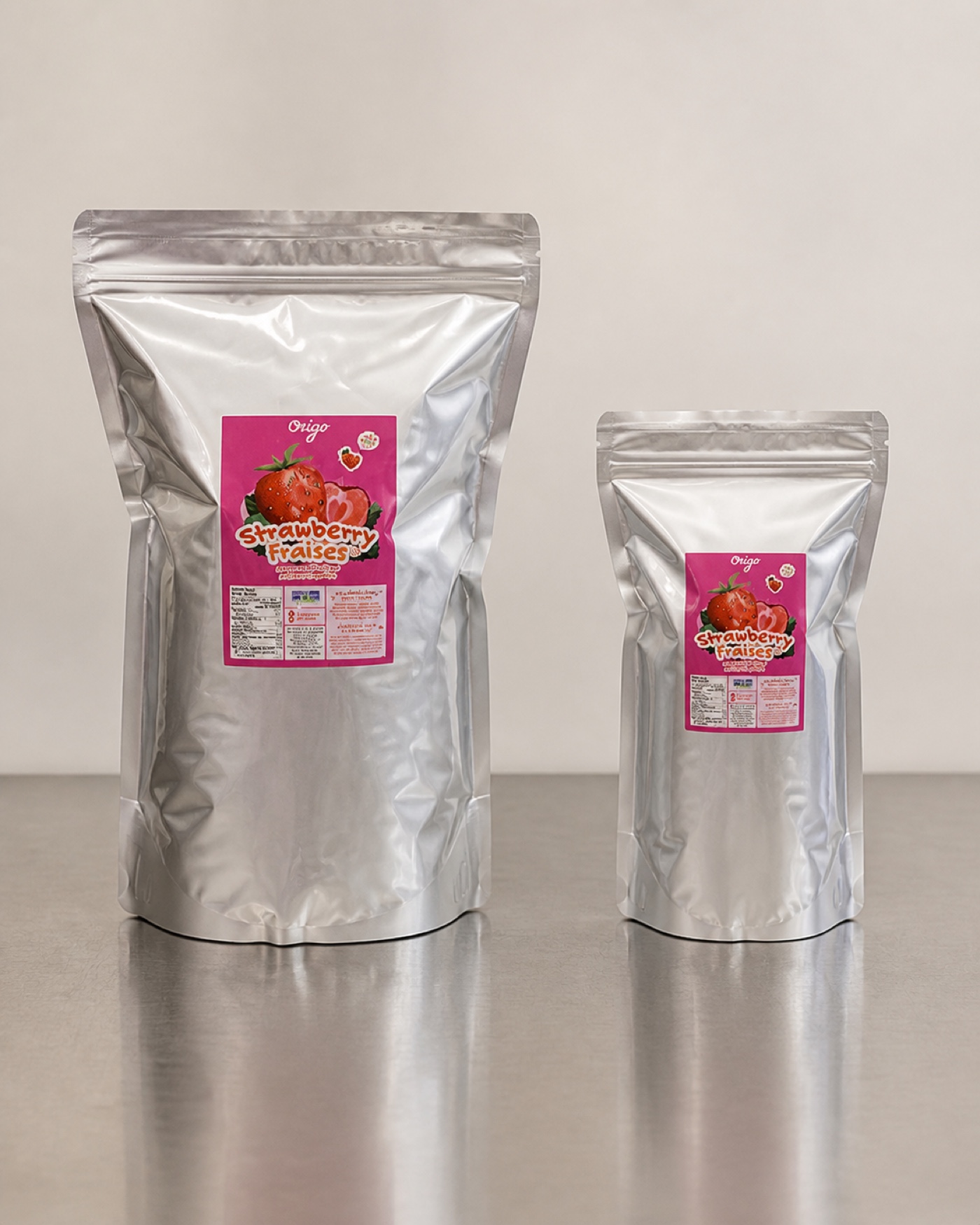Origo large and small wholesale freeze-dried strawberry pouches standing side by side on a stainless steel bench, showing their true relative size